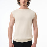 Man wearing a beige sleeveless shirt and black pants on a white background