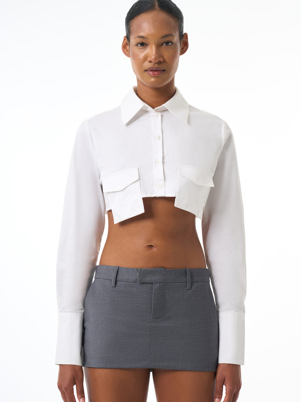 Woman wearing a white cropped shirt and gray skirt on a white background