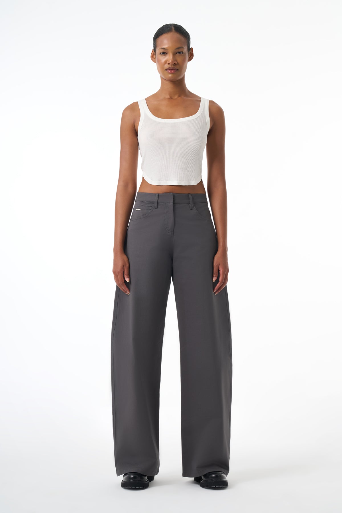 Woman wearing a white tank top and gray pants on a white background