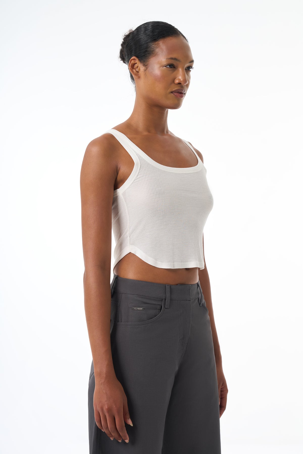 Woman wearing a white tank top and gray pants on a white background