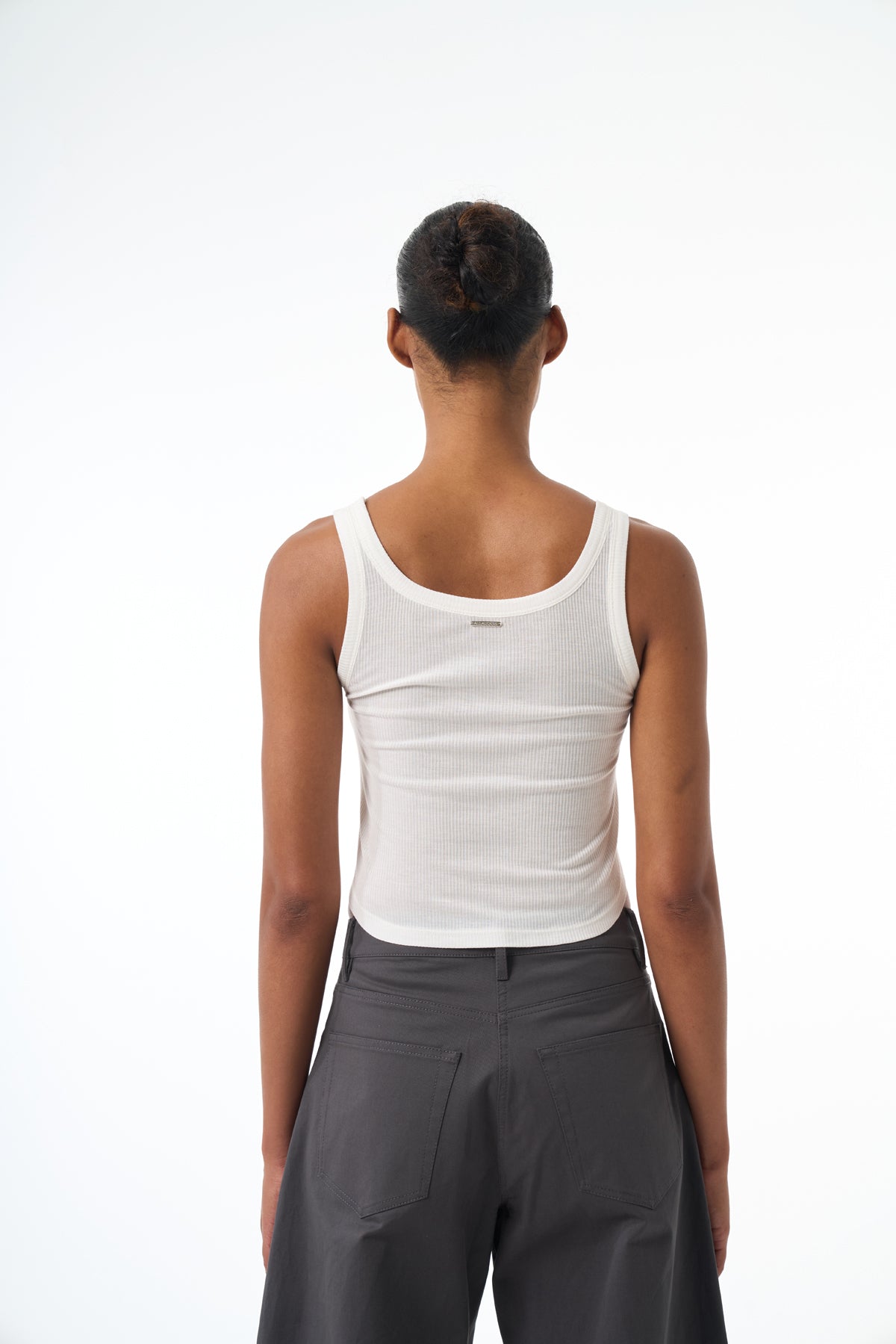 Woman wearing a white tank top and gray pants on a white background