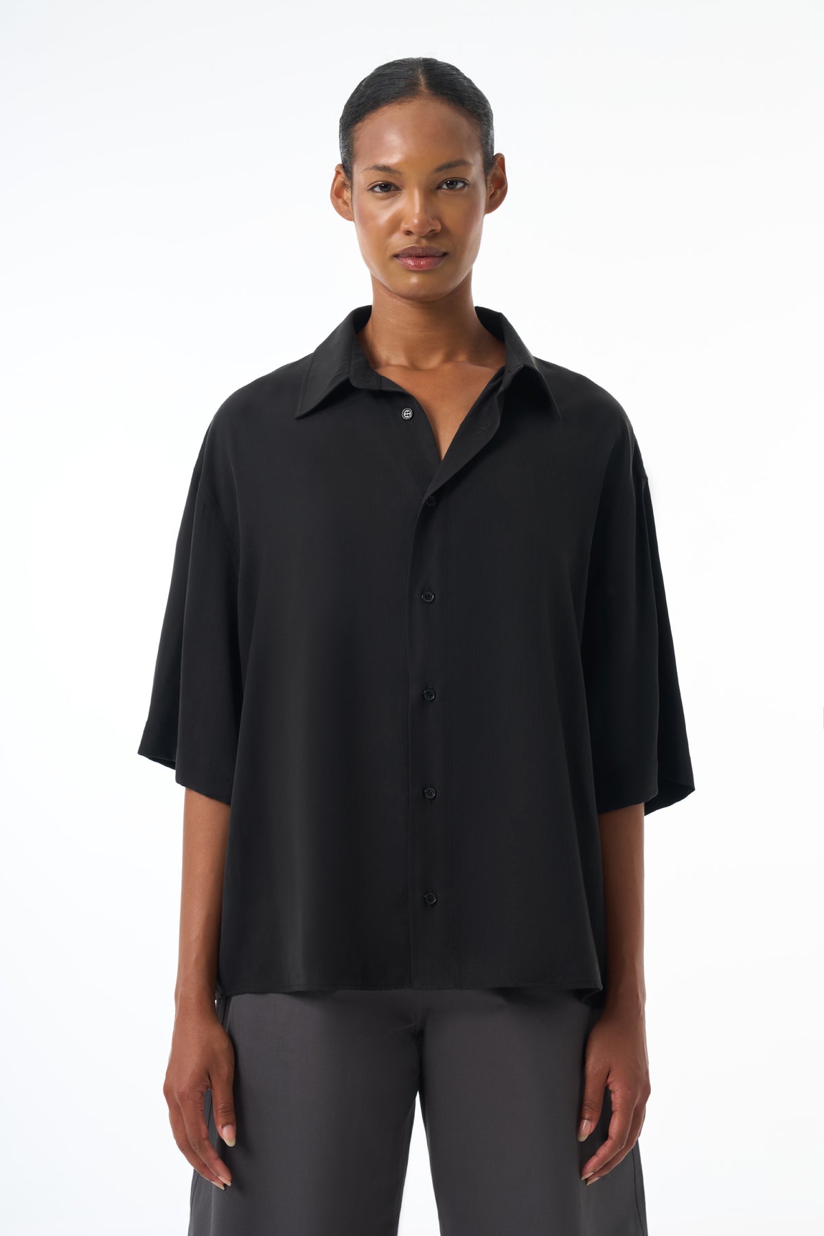 Woman wearing a black button-up shirt and gray pants on a white background