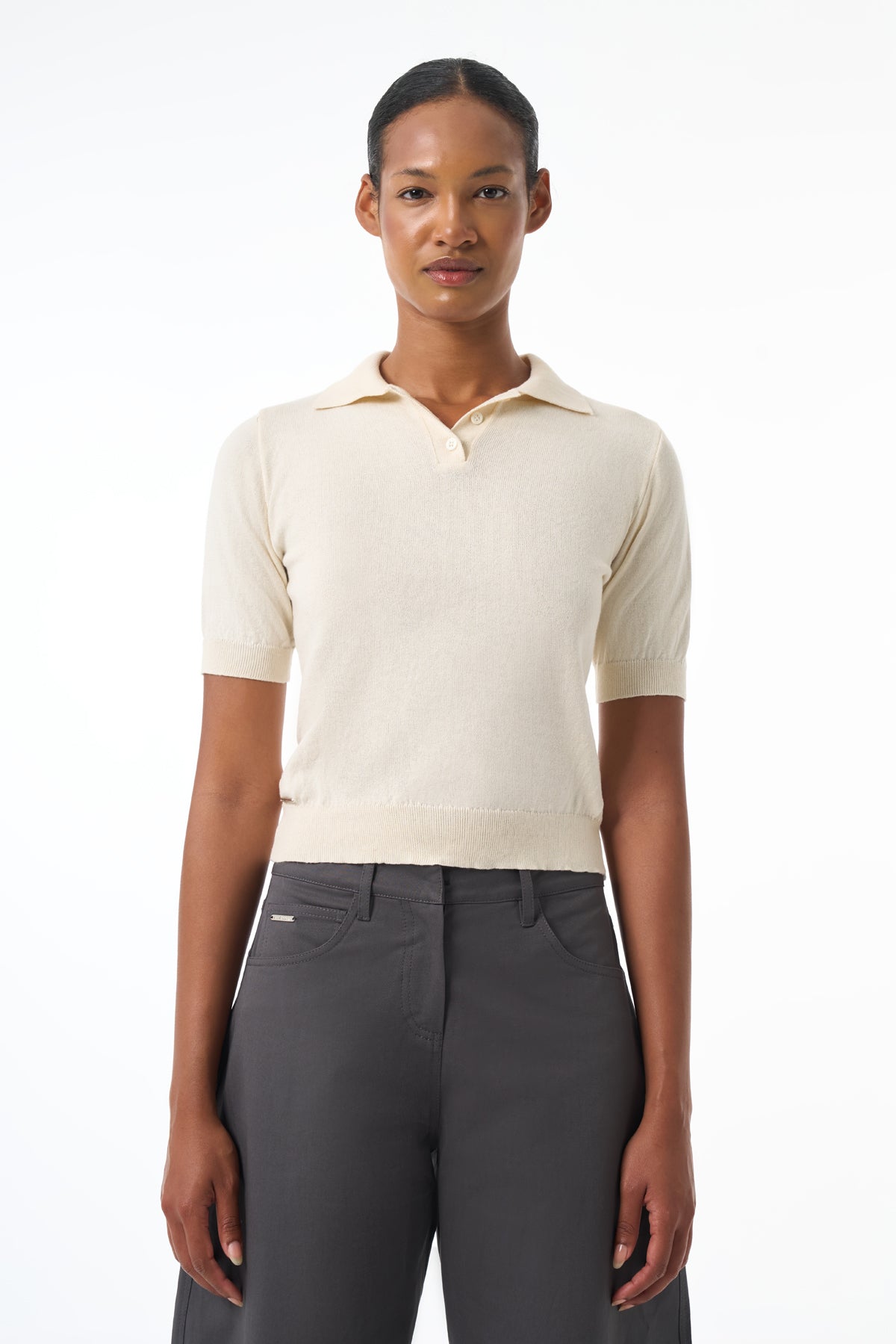 Woman wearing a cream-colored short-sleeve shirt and gray pants on a white background