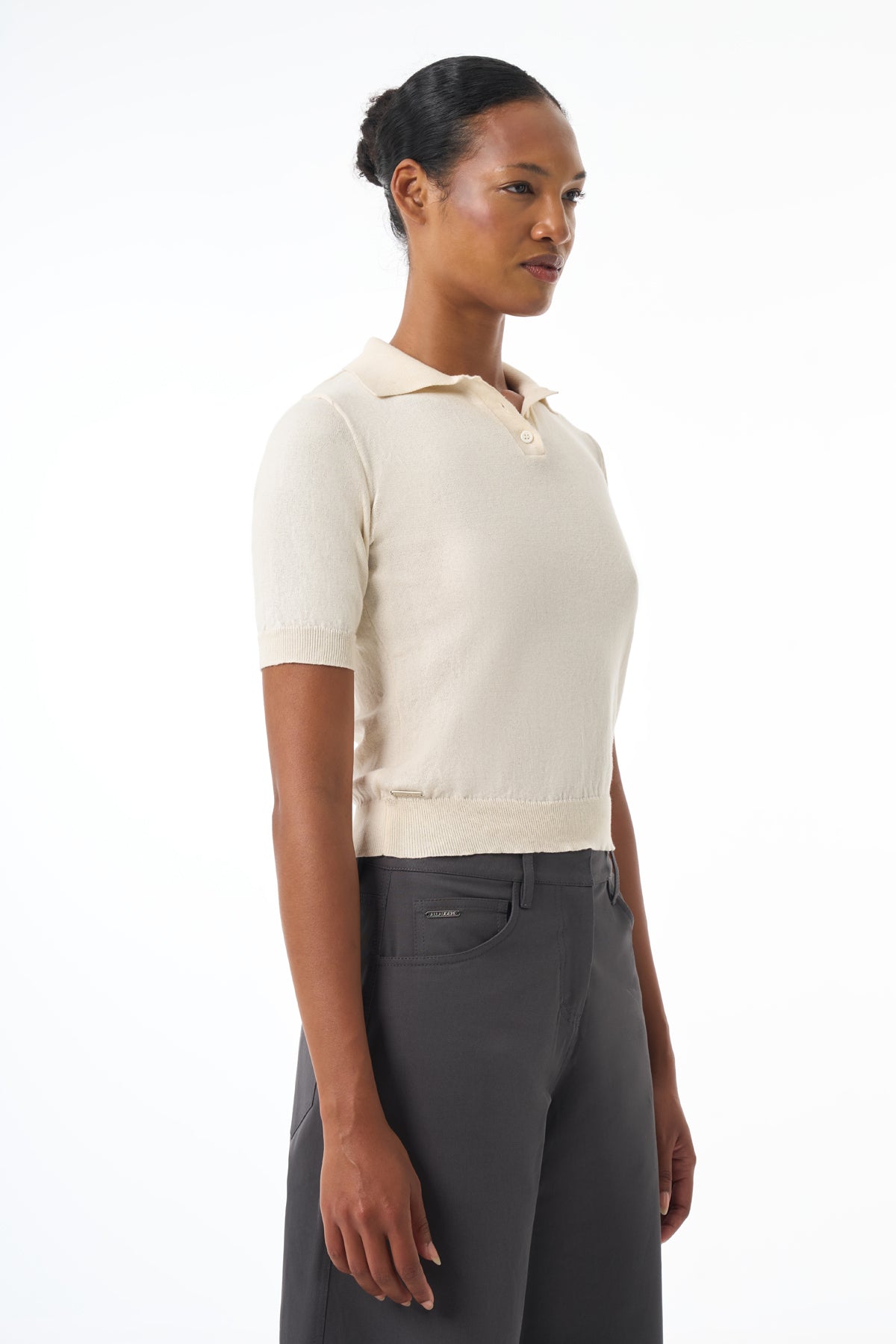 Woman wearing a beige short-sleeve knit shirt and gray pants on a white background