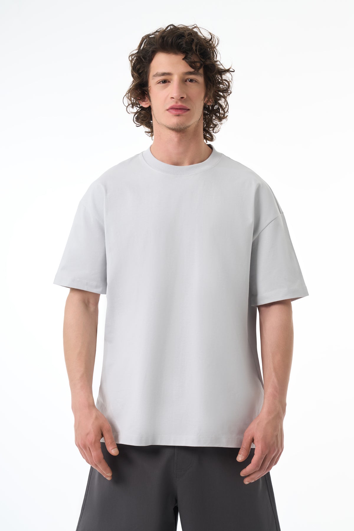 Man wearing a light gray t-shirt and dark pants on a white background