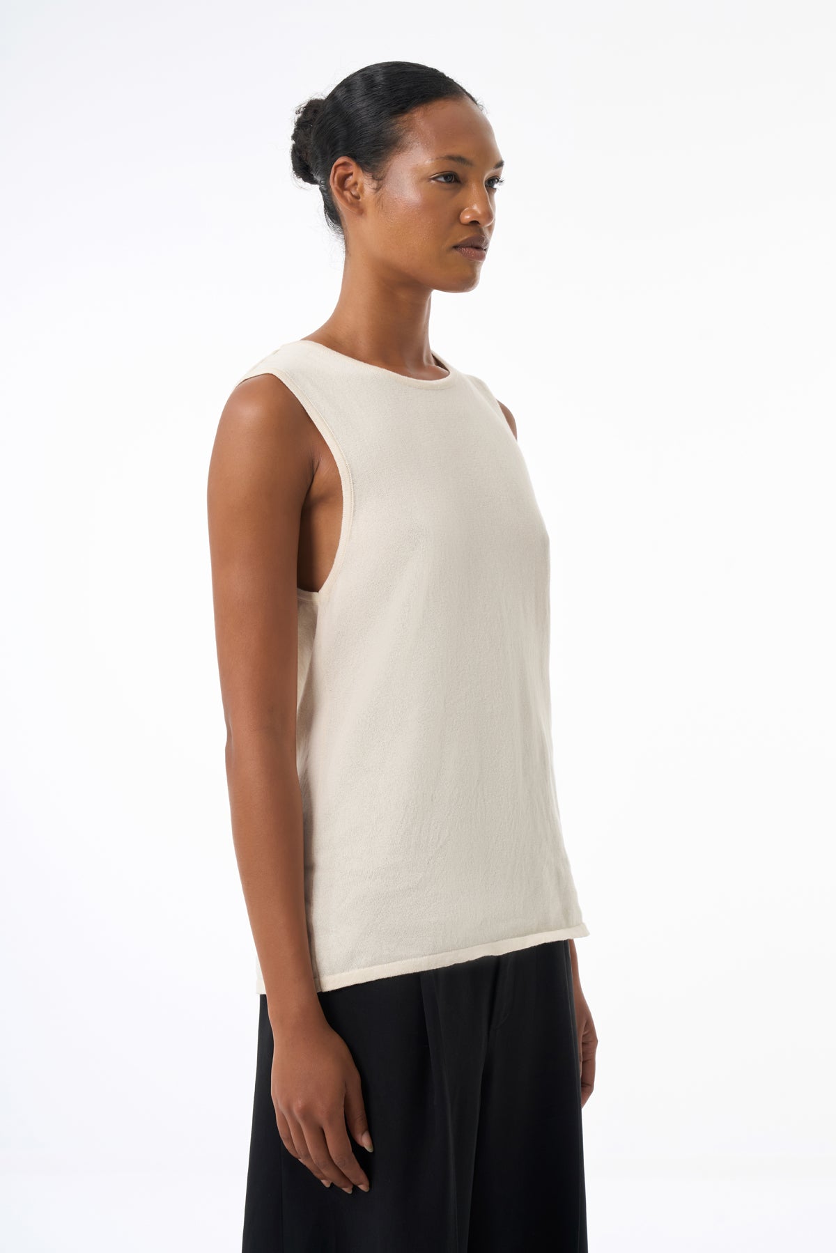 Woman wearing a white sleeveless top and black pants on a white background
